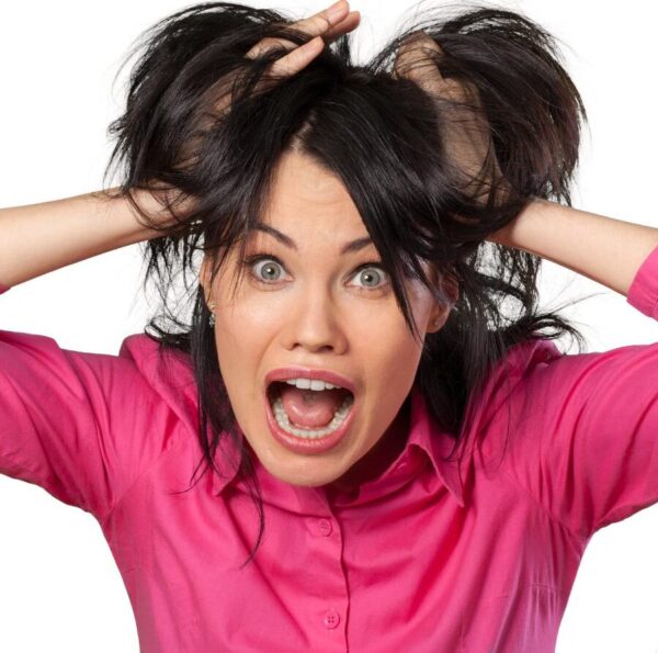 Women in bright pink shirt put both of her hands to her head and pushing up her hair as in a panic state and her mouth is wide open. she represents a women in a stressed state about her hair.