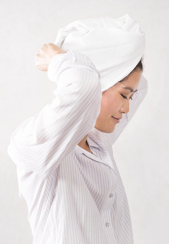 Woman's hair in a white Lilla Rose bamboo hair towel. We see her from her profile; her hands are behind her head, securing the hair towel for the article The importance of taking care of your hair when you are stressed.  