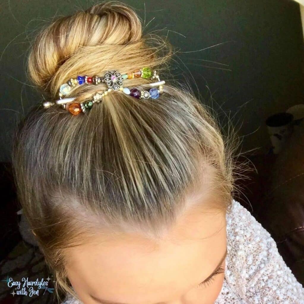 Women in a white sparkle shirt only shows half her face, forehead, and one closed eye being shown on an angle. Her blonde hair is pulled back tight into a bun secured by a Lilla Rose Flexi Clip in the front of the bun. The Flexi Clip is multi-colored She is in front of a black background.under the heading Lilla Rose Accessories-What are they for the article Get Your Hair Game On Point with Lilla Rose Accessories - Say Goodbye to Bad Hair Days!