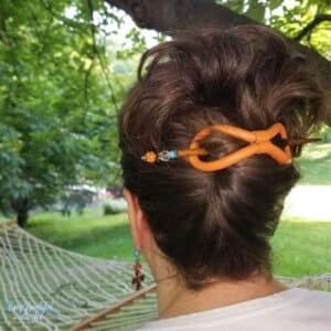 Back of women's head with her hair up in a messy twist held up by a Lilla Rose leather eight and hair stick in orange. She is outside facing an hammock in the article10 tips for maintaining healthy hair. 